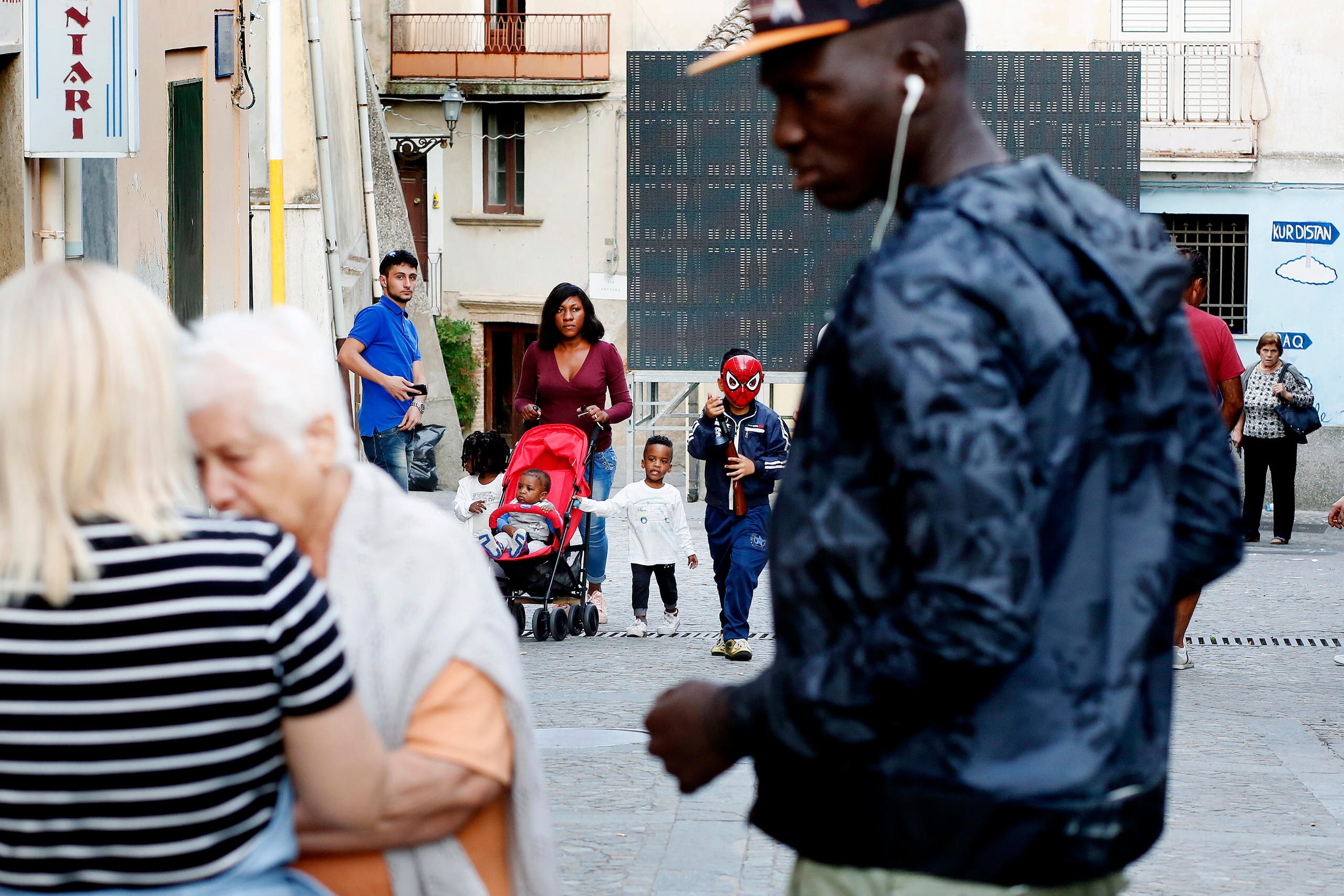 Persone a passeggio nelle strade di Riace, con un uomo di colore in primo piano