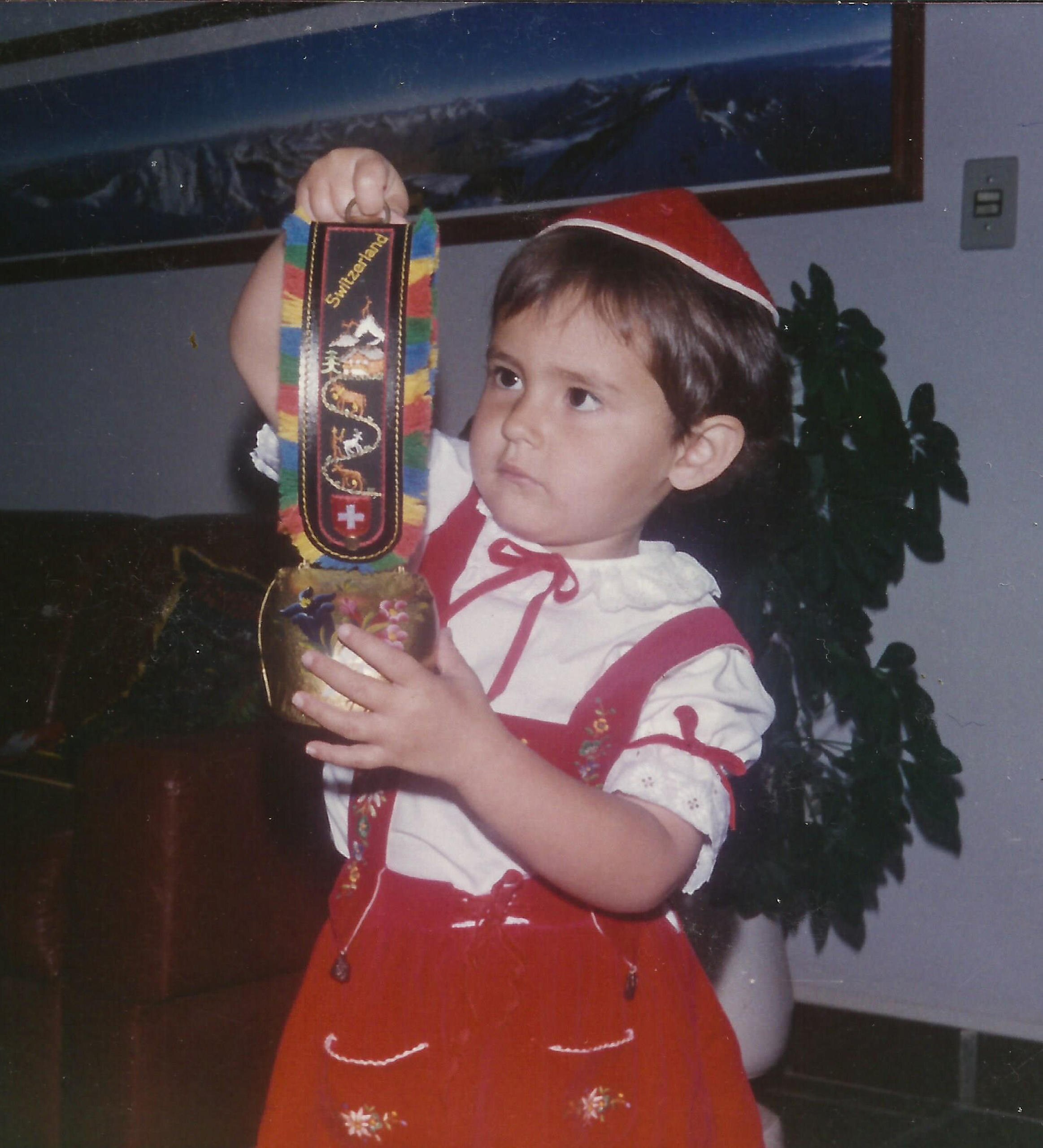 bambina che indossa un costume tradizionale e tiene in mano una campana decorata.