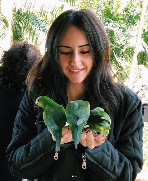 una donna con tre pappagalli verdi che mangiano dalle sue mani