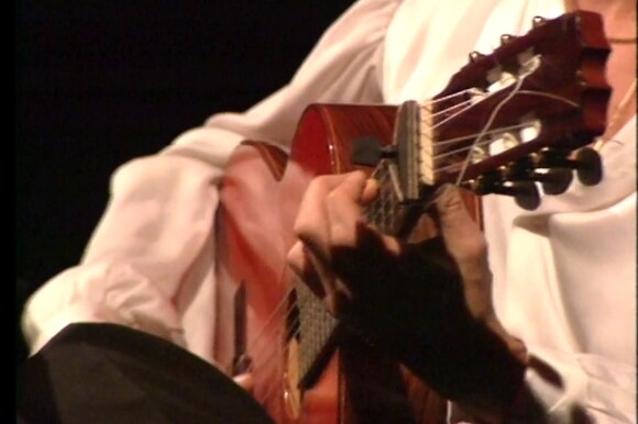 Primo piano sulla chitarra imbracciata da Paco De Lucia, che indossa tipica camicia bianca e pantalone nero (flamenco)