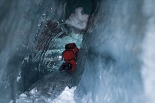 Un uomo striscia attraverso uno stretto tunnel ghiacciato a quattro zampe
