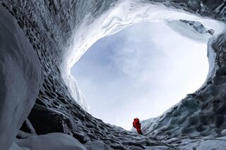 Visto dal basso, un uomo si trova sul bordo di un grande buco nel ghiacciaio