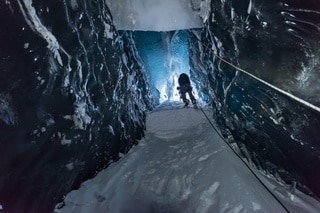 Uomo si arrampica su per un pozzo nel ghiacciaio, visto dal basso