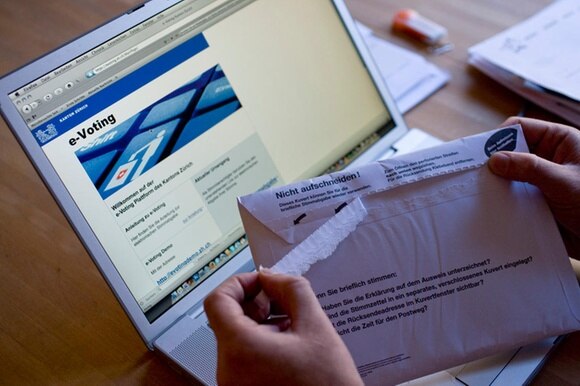 Qualcuno apre una busta con il materiale di voto davanti a un laptop, sul cui schermo si vede la pagina del voto elettronico.