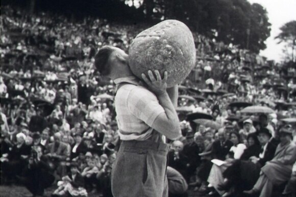 Historic photograph of a man lifting up a 83.5 kilogram stone