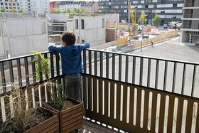 Ein Junge steht auf einem Balkon und schaut auf eine grosse Baustelle hinunter.