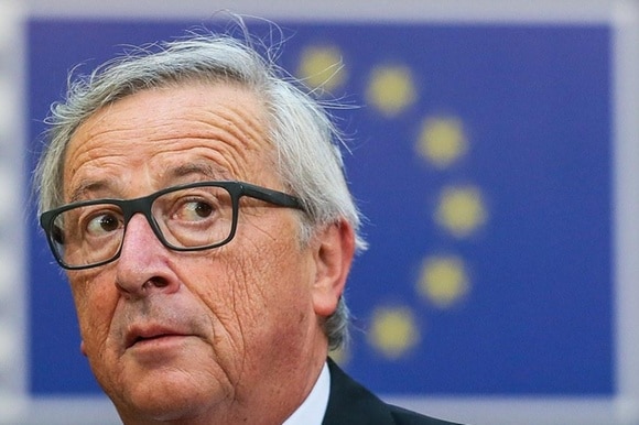 Primo piano del volto di Jean-Claude Juncker e sullo sfondo la bandiera europea.