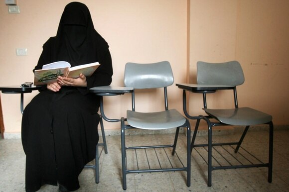 Una donna completamente velata, seduta,tiene in mano un libro