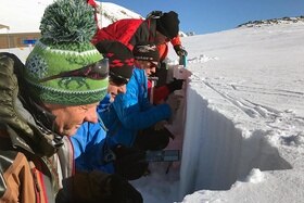 quattro uomini in tuta da sci esaminano la sezione del manto nevoso