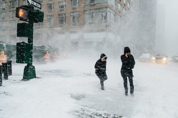 Due persone attraversano la strada investite da vento e neve, a un incrocio di New York