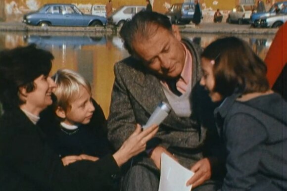 Gianni Rodari intervistato da una ragazzina. Nella foto anche un piccolo spettatore e una giornalista adulta.
