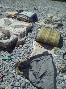 Un materasso, un sacco a pelo e delle coperte sui sassi lungo un fiume a Ventimiglia.