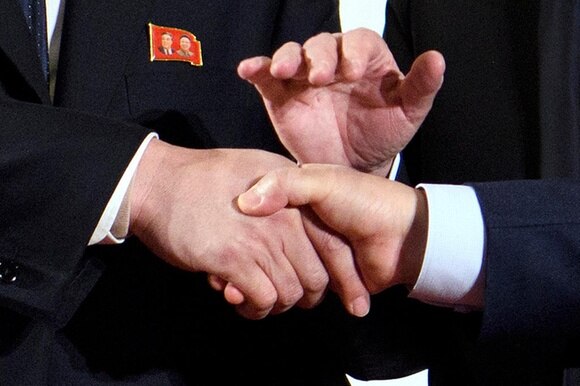 Grossaufnahme eines Handschlags, eine dritte Hand liegt auf den beiden Händen.
