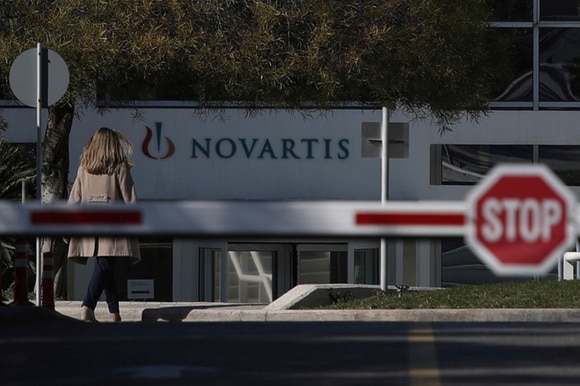 Una donna si dirige, forse al lavoro, negli uffici della Novartis di Atene. In primo piano, una barra con segnale Stop