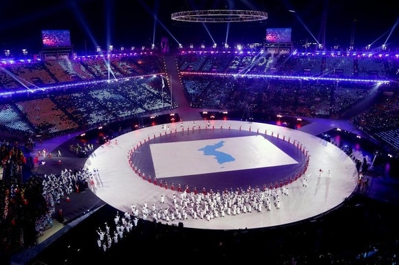 Un anello illuminato di bianco al centro di uno stadio sul quale sfila la delegazione di atleti coreani.