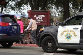 Due anziani camminano nei pressi di un auto della polizia accanto al cartello Veterans Home of California