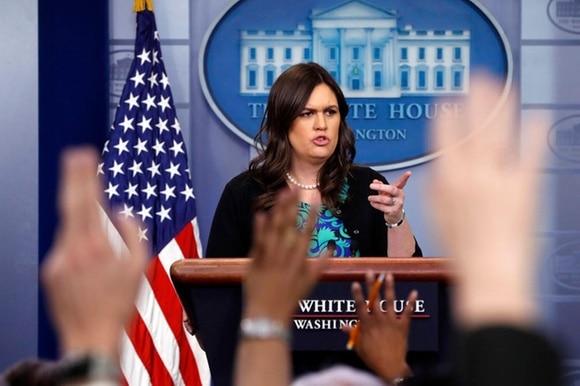 La portavoce della Casa Bianca al pulpito di fronte a giornalisti con la mano alzata, dà la parola a uno di essi