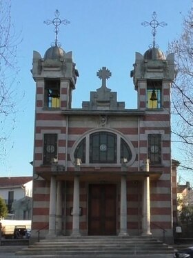 Facciata di una chiesa stile liberty con due guglie e rosone, albero spoglio a destra.