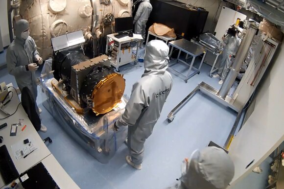 Il satellite circondato da tre scienziati vestiti di tuta, guanti e mascherina in una stanza appositamente isolata