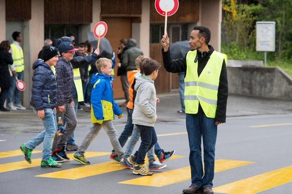 Richiedenti l asilo aiutano degli scolari ad attraversare la strada.