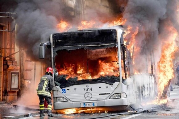Un pompiere intento a spegnere le fiamme di un bus che ha preso fuoco in pieno centro di Roma