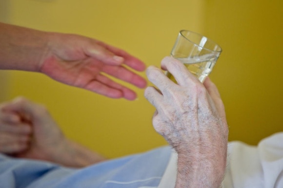 La mano di un giovane porge un bicchier d acqua alla mano di un anziano
