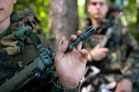 una mano di un soldato è posata sulla canna di un fucile di assalto