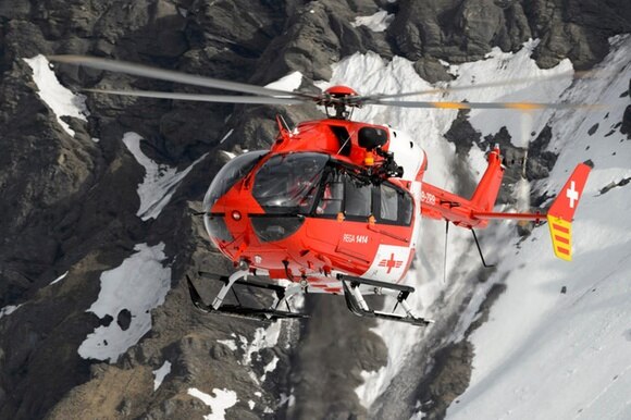 elicottero della Rega in volo davanti a una montagna