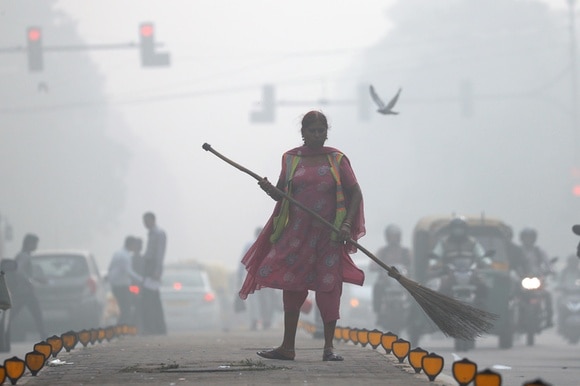Eine Frau steht mit einem Besen auf einer Strasse, wegen des Smogs sieht man sie kaum.