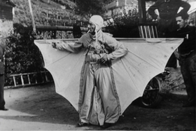 Uomo vestito con una strana tuta che ha cucite sui fianchi due ali a mo di pipistrello (o deltaplano)