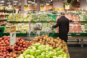 Un uomo con un carrello della spesa in mezzo agli scaffali di frutta e verdura in un supermercato