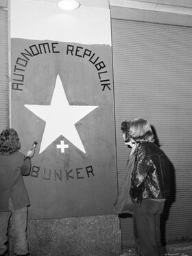 due giovani dipingono un cartello con la scritta: Autonome Republik Bunker