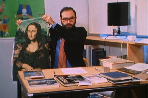 Umberto Eco, nel suo studio, mostra un grembiule con stampata la Gioconda; libri sulla scrivania