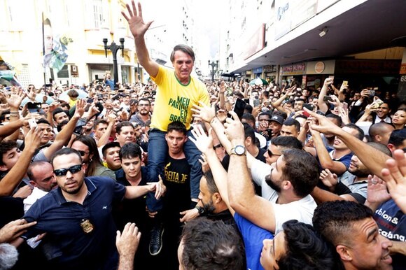 Uomo con maglietta verdeoro sulle spalle di un ragazzo, attorniato da folla acclamante con le braccia alzate