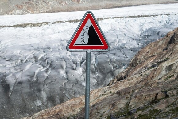 cartello con pericolo cadute massi e sullo sfondo un ghiacciaio