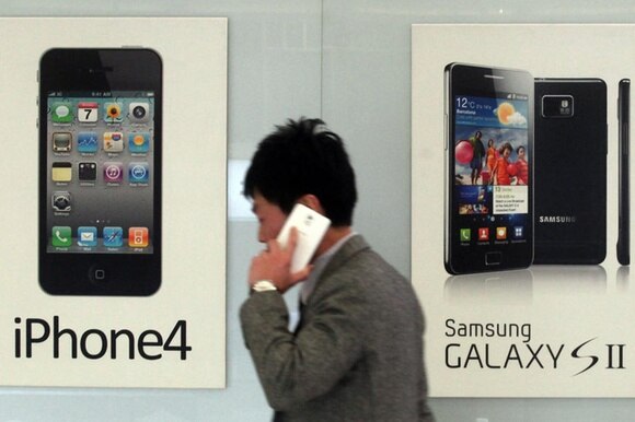 uomo con telefono cammina davanti a due cartelloni pubblicitari iphone e samsung
