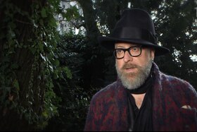 [fotogramma del video] Primo piano di Mario Biondi ripreso all ombra di alcuni alberi; indossa cappello nero