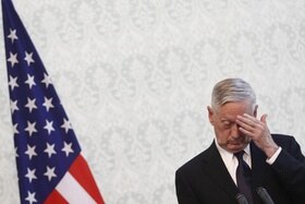 Jim Mattis, al margine dx della foto, guarda in basso e si tocca la fronte; sulla sx, bandiera statunitense