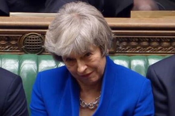 Primissimo piano di Theresa May con blazer blu, seduta alla Camera dei Comuni
