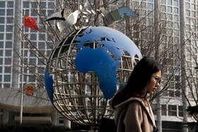 Ragazza, di profilo, passa accanto a una scultura del pianeta Terra davanti alla sede del ministero degli esteri cinese