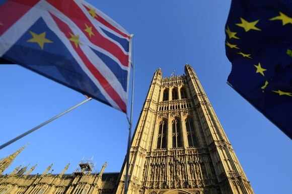Vista dal basso di una torre di Westminster con, in primo piano, parti di una bandiera UE e una britannica con stelle