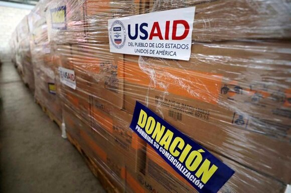 Primo piano di scatoloni rivestiti da cellophane con autoadesivi che riportano le scritte USAID e Donación