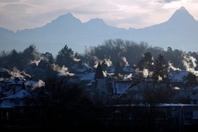Sicht übers Mittelland auf die Berge, im Vordergrund viel Rauch aus Kaminen