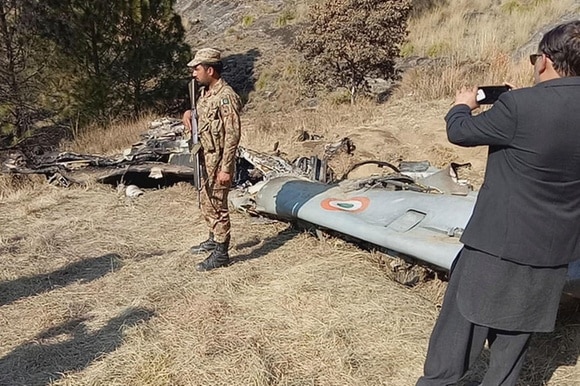 Carcassa di un aereo (si distingue l ala) in un bosco, con un militare di guardia; un uomo in abito scatta una foto