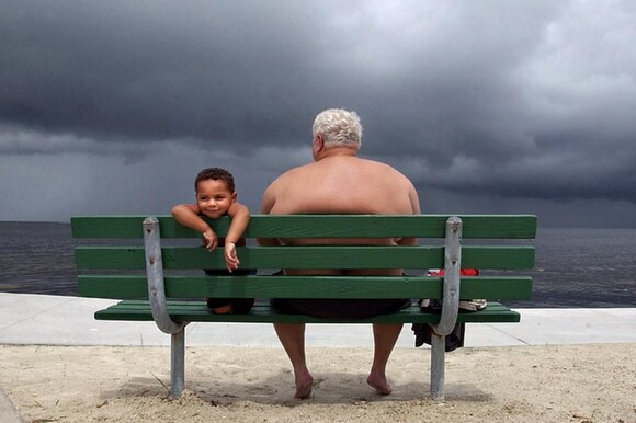 Un anziano e un bambino seduti su una panchina in riva al mare.