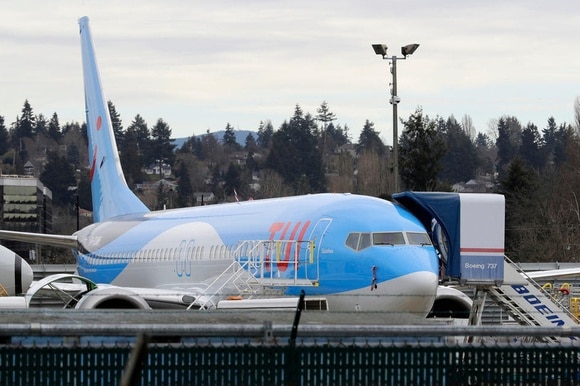 Immagine di un aereo con logo TUI scattata da dietro una rete metallica; si vede scaletta con scritta Boeing