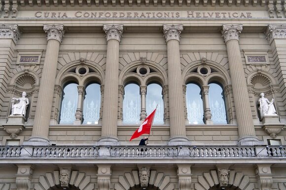 Vista della facciata di Palazzo Federale con vetrate centrali e bandiera svizzera, si intravvedono gli archi dei portali
