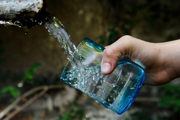 mano che riempie un bicchiere con l acqua di una fontana