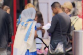 Immagine sfocata di una donna con velo e un uomo mediorientale che parlano insieme, per strada