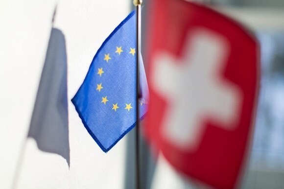 Bandierina dell UE (a fuoco) e dietro di essa bandiera svizzera (sfocata) su fondo non ben definito